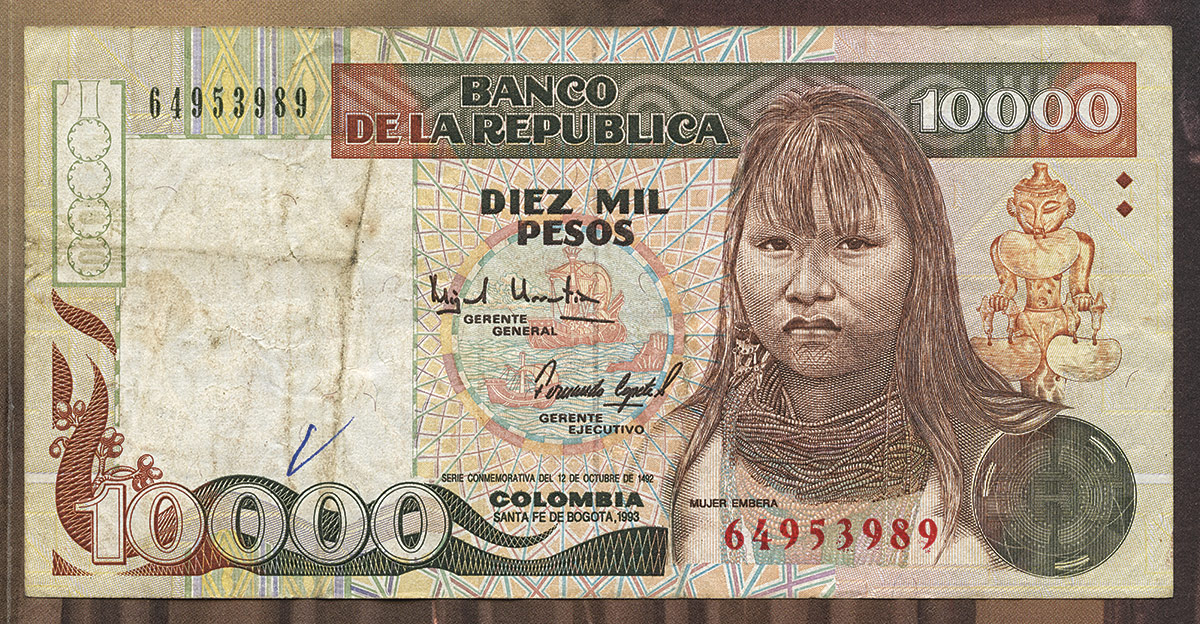 Detalle de un billete de 10.000 pesos colombianos, 1992. La serie a la que perteneció este ejemplar fue conocida como «segunda familia de billetes» y quienes los ilustraron fueron comisionados para reemplazar a los antiguos próceres. El diseño inicial fue realizado por Liliana Ponce de León; sin embargo, el rostro de la mujer emberá propuesto por ella no quedaría en el billete definitivo. La artista colombiana declaró: «Entendí que era un billete sin fortuna […] Un año después de su aparición al público hubo un robo millonario y desaparecieron todas las planchas de impresión, seguido de la aparición de millones de loritos forajidos que volaban por todas partes sin oro en ningún socavón». Apenas dos años después de su emisión, el billete de 10.000, junto al de 5.000 y al de 2.000 pesos, tuvo que ser sacado de circulación luego del llamado «robo del siglo», ocurrido en Valledupar en 1995.