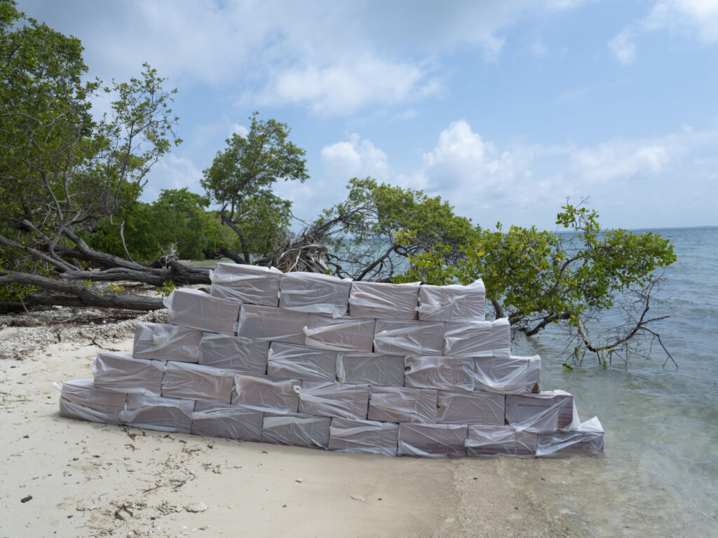 «Cargo». Isla Palma, Bolívar. Octubre, 2021. Un cargamento de cocaína apilado a la orilla del mar esperando ser recogido por una lancha rápida. Esta fue una de las intervenciones que más preparación requirió, no por su complejidad, sino porque debíamos conseguir los ladrillos, conseguir una embarcación que soportara el peso y pudiera transportar la carga hasta la isla lejos de la línea de playa. Junto a Deivis Vecino del Mar y Federico Martínez, vivimos varios sustos por culpa del oleaje que pegaba a veces con fuerza desviando el muro improvisado: se partieron varios ladrillos y se perdieron algunos cauchos, que tuvimos qué reponer a "la seño" que nos los había prestado. Foto de <b>Santiago Escobar-Jaramillo</b>.