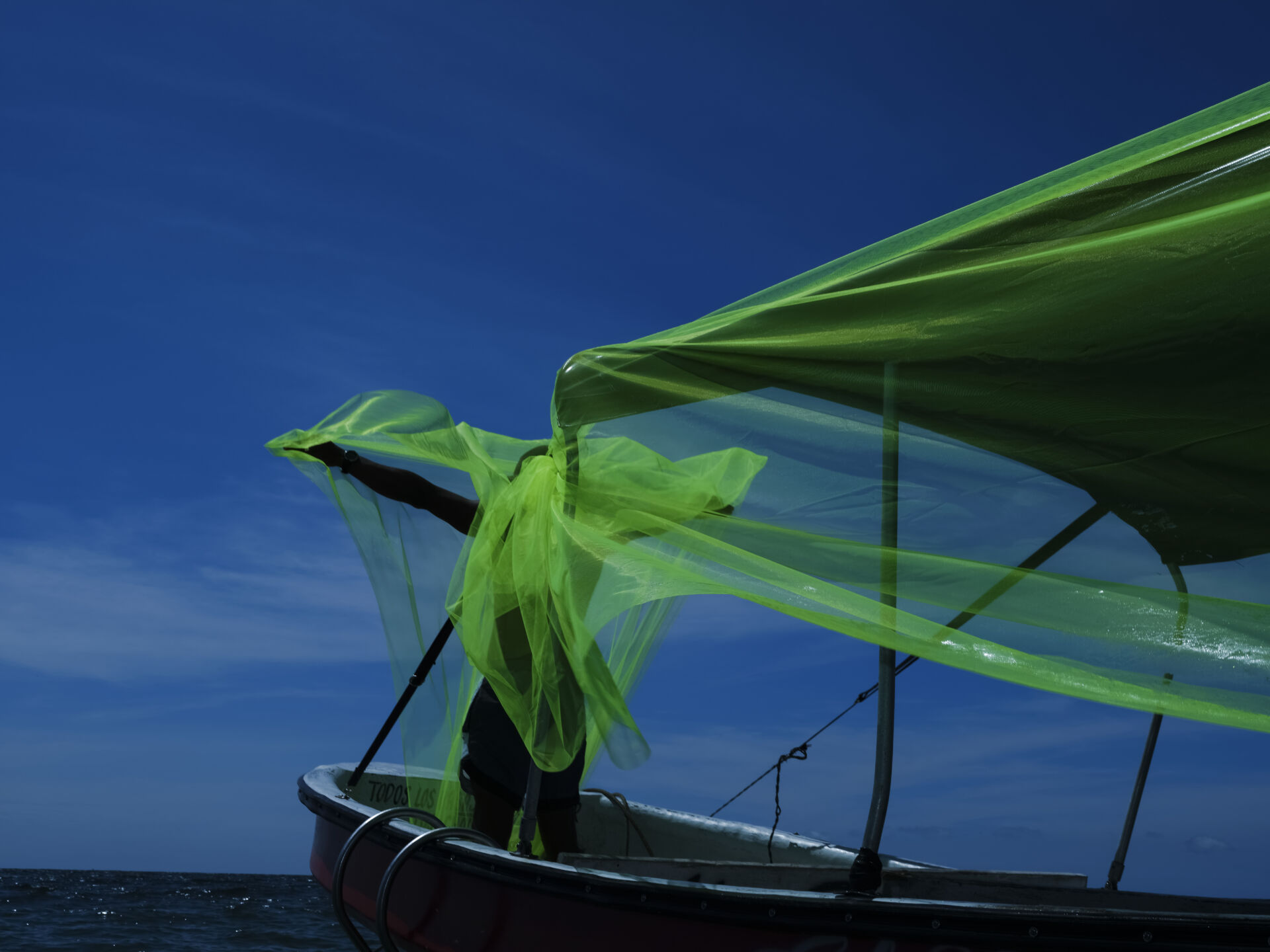 «Lancha rápida». Rincón del Mar, Sucre. Octubre, 2021. Intervención paisajística utilizando tela verde, una lancha y un personaje con los brazos abiertos como un pez volador hacia el horizonte. Foto de Santiago Escobar-Jaramillo.