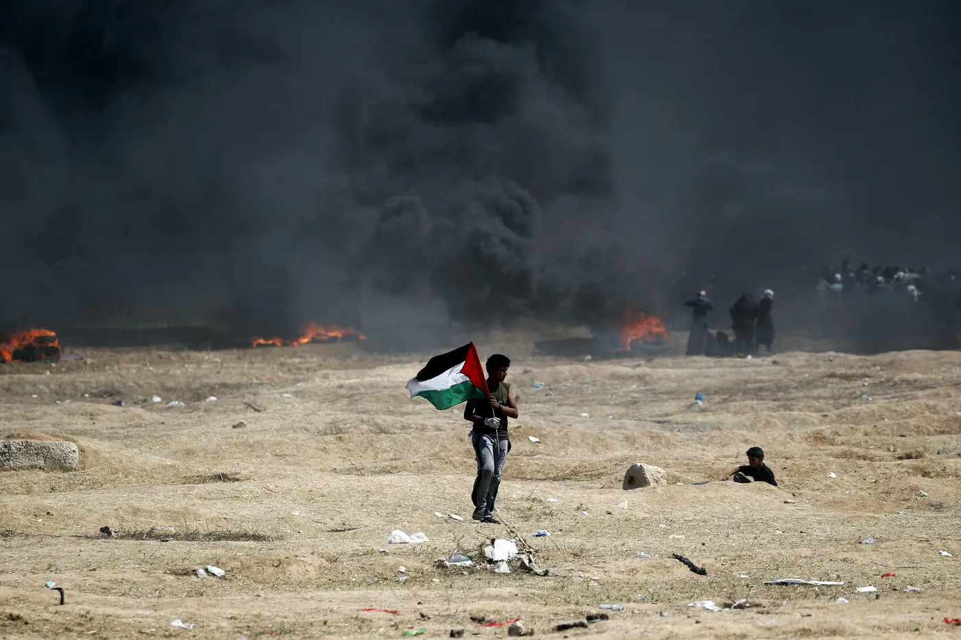 Un hombre sostiene una bandera palestina durante los enfrentamientos con las fuerzas israelíes cerca de la frontera entre la Franja de Gaza e Israel, al este de la Ciudad de Gaza, el 14 de mayo de 2018, tras el controvertido traslado de la embajada de Estados Unidos a Israel. Foto: Thomas Coex (AFP).