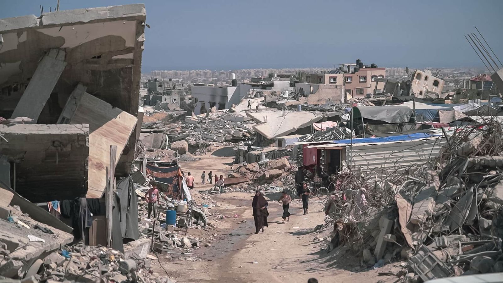 Zona urbana devastada en Gaza con escombros, edificios colapsados y personas caminando entre las ruinas. Foto: Jaber Jehad Badwan.